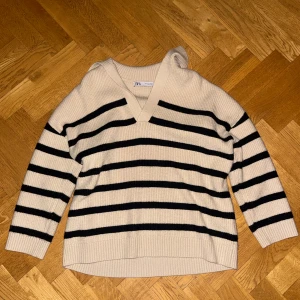 Randig beige stickad tröja från Zara - Säljer en beige stickad tröja från Zara i storlek S med svarta ränder. Tröjan har v-ringad hals och långa ärmar, samt ribbade muddar vid ärmslut och nederkant. Andvänd endast fåtal ggr. Pris kan diskuteras.