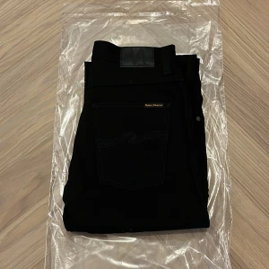 Helt nya Nudie jeans co - slim Jim - W32 L32 - Helt nya och oanvända Nudie Jeans Co Slim Jim i färgen Dry Black – fortfarande i originalförpackning (se bilder).  En tidlös och elegant modell i helsvart rådenim med perfekt balans mellan klassisk passform och modern stil.  Detaljer: • Modell: Slim Jim • Storlek: W32 / L32 • Färg: Dry Black (matt svart rådenim) • Passform: Regular slim – normal midja, lätt avsmalnande ben