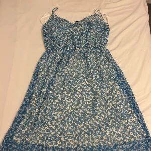 Blommig blå kort klänning Vero Moda - Supersöt kort klänning från Vero Moda i blått och vitt med blommigt mönster. Klänningen har smala axelband, markerad midja och ett luftigt, flowy tyg som känns perfekt för varma dagar. Materialet är lätt och mjukt, vilket gör den extra skön att bära. Köpt för 600