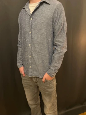 Blå linneskjorta från Jack & Jones - Snygg blå skjorta från Jack & Jones i mjukt linnematerial. Klassisk krage, vita knappar och långärmad modell. Skjortan har en avslappnad passform och passar perfekt till jeans eller chinos. Enkel och stilren design som funkar året runt.