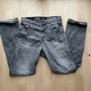 Replay grå jeans  - Snygga grå jeans från Replay med klassisk femficksdesign och raka ben. Jeansen har svarta broderade detaljer på bakfickorna och Replay-logga på myntfickan. Materialet är mjukt denim i bomull och passformen är normal med midwaist.