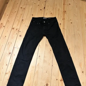 Svarta jeansbyxor från Dressmann - Svarta jeansbyxor från Dressmann med klassisk femficksdesign och raka ben. Byxorna har knapp och dragkedja framtill samt två bakfickor. Materialet är jeans med en mjuk känsla och passformen är normal. Perfekt för dig som gillar stilrena och enkla svarta jeans.