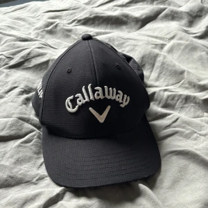 Svart Callaway keps - Snygg svart keps från Callaway med vit broderad logga framtill. Klassisk böjd skärm och strukturerad form som sitter skönt på huvudet. Perfekt för golf eller chill dagar utomhus. Justerbar baktill för bästa passform.