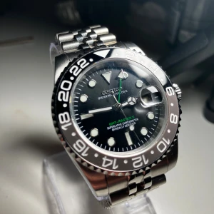 Seiko GMT - Bruce Wayne - Seiko GMT med jubilee länkar. Caseback i glas (så man ser urverket), automatiskt NH35 urverk. Klockan är byggd med delar i hög kvalité och är vattentät.