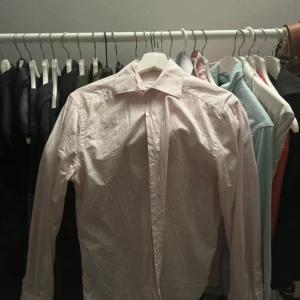 Rosa randig skjorta These Glory Days - Snygg rosa och vit randig skjorta från These Glory Days i italienskt bomullstyg. Klassisk krage, långärmad och med knappar framtill. Perfekt för dig som gillar stilrena och fräscha plagg med en modern touch.