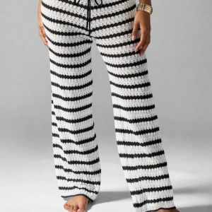 Randiga stickade byxor med snörning - Snygga stickade byxor med svartvita ränder och dragsko i midjan. Byxorna har en loose passform och raka ben, perfekta för en chill och trendig look. Materialet är stickat och känns mjukt mot huden. Kombinera med matchande topp för en hel outfit använda en gång under semester .