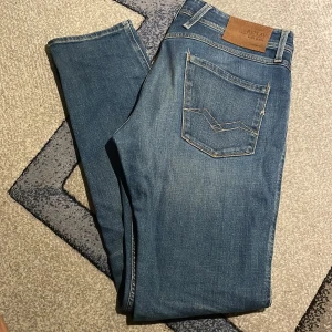 Blå Replay Anbass jeans - Säljer ett par snygga Replay Anbass jeans i klassisk blå tvätt. Jeansen har fem fickor, coola kontrastsömmar och läderpatch bak i midjan. Modellen är slim och materialet är mjukt denim med lite stretch för extra komfort. Anbass 34W34L säljer för jag aldrig använder dem. Max använda 10 gånger skick 9/10