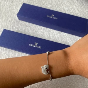 Swarovski armband med säl - Supersött armband från Swarovski i silverfärg med en gnistrande säl-berlock täckt av små kristaller. Tunn kedja med flera små glittriga detaljer och justerbar längd. Perfekt för dig som gillar unika och lekfulla smycken med extra bling. Box och presentkvitto finns