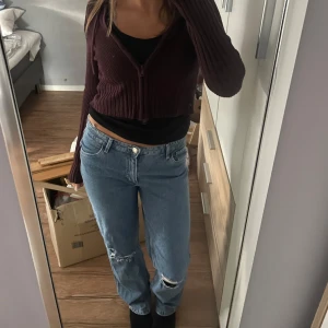 Blå straight jeans från H&M - Säljer ett par blåa straight fit jeans från H&M med låg midja och justerbar midja. Jeansen har slitna detaljer vid knäna och klassisk femficksdesign. Perfekta för en avslappnad och trendig look.