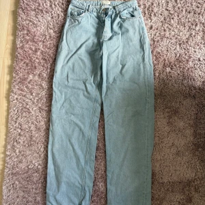 Ljusblå jeans från Lis Bonne Atelier - Säljer ett par ljusblå jeans från Lis Bonne Atelier med klassisk femficksdesign och guldfärgad broderad logga på fickan. Jeansen har raka ben och normal passform, tillverkade i mjukt denimtyg med silverfärgade knappar framtill.
