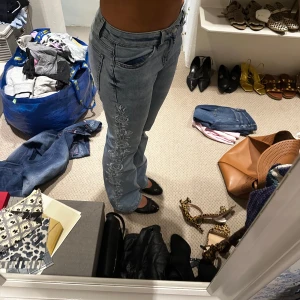 Coola jeans - Säljer ett par ljusblå jeans med snyggt broderade rosor längs utsidan av benen. Jeansen har normal passform, raka ben och klassisk femficksdesign.  Mått: Midja: 36cm Innerbenet: 21cm Längd: 100cm Använda fåtal gånger