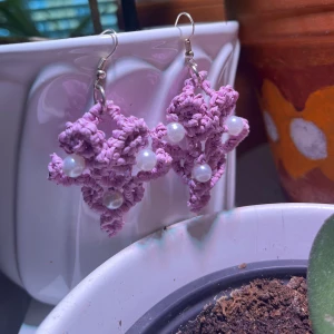 Handgjorda lila örhängen med pärlor - Unika handgjorda örhängen i lila med tre vita pärlor. De har en snygg, blomliknande form och hängs på klassisk krok. Perfekta för dig som vill sticka ut med ett kreativt och färgglatt smycke.