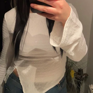 Vit omlottopp med vida ärmar - Säljer en vit omlottopp med lång, vid ärm och strukturerat tyg. Toppen har en asymmetrisk nederkant och är tillverkad i ett lätt, skönt material. Perfekt för dig som gillar stilrena och trendiga plagg.