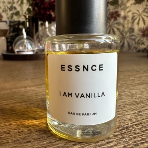 ESSNCE I Am Vanilla - Parfymflaska från ESSNCE med doften I Am Vanilla. Flaskan är rund och genomskinlig med svart lock och vit etikett. Innehållet är gyllengult och flaskan har en stilren, minimalistisk design. Perfekt för dig som älskar söta och varma vaniljtoner.