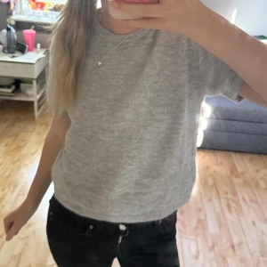 Grå stickad kortärmad topp - Mysig grå stickad topp med korta ärmar och rund halsringning. Modellen är croppad, perfekt att styla med jeans eller kjol. Storlek 158/164.