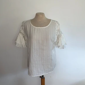 Vit blus med spets från Esprit - Supersöt vit blus från Esprit med tunna vertikala ränder, volangärmar och spetsdetaljer på axlarna. Blusen har rund halsringning och knappar i ryggen. 