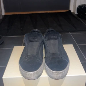 Svarta sneakers från Axel Arigato - Säljer ett par svarta sneakers från Axel Arigato med stilren design och slip-on modell. Skorna har en tjock vit platt sula och är tillverkade i mocka med diskret logga på sidan. Perfekt för dig som gillar minimalistisk och modern stil. Köpta för 2500 använda ganska mycket och är ett litet håll i sulan men påverkar inte skorna eller dina strumpor,inget som läcker 