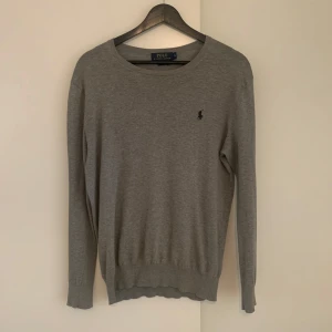 Grå slim fit tröja från Polo Ralph Lauren - Snygg grå tröja från Polo Ralph Lauren i slim fit-modell. Tröjan har rund halsringning, lång ärm och den klassiska broderade loggan på bröstet. Tillverkad i mjuk bomull med inslag av kashmir för extra komfort. Tröjan är i gott skick och inte andvänd särskilt mycket