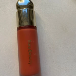 Rare Beauty Joy flytande rouge - Lite slarvigt använd, men ny! Säljer Rare Beauty Liquid Blush i färgen Joy, en varm persikoton som ger fräsch lyster till kinderna. Kommer i en snygg frostad flaska med guldlock och har en lätt, krämig formula som är enkel att blanda ut. Perfekt för dig som vill ha naturlig glow.