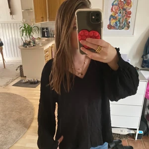 Svart blus med v-ringning och volymärm - Säljer en svart blus med v-ringning och lätt volym i ärmarna. Blusen har en luftig passform och diskret struktur i tyget. Perfekt att styla med jeans eller kjol för en chill och snygg look.