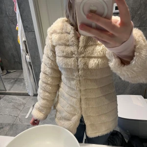 Beige pälsjacka med fluffig look - Supermjuk och fluffig beige pälsjacka med horisontella sömmar som ger en cool struktur. Jackan har lång ärm och är perfekt för dig som vill ha en mysig och trendig vibe. Passar till jeans eller klänning för en chill men snygg stil.
