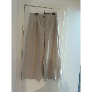 Beiga vida byxor i linmix - Snygga beiga byxor med hög midja och vida ben. Byxorna har knäppning fram och diskreta fickor. Perfekta för en chill och stilren look, lätta och luftiga i materialet.