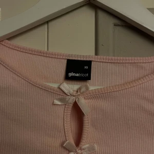 Ljusrosa ribbad topp med rosetter Gina Tricot - Supersöt ljusrosa ribbad topp från Gina Tricot med långa ärmar och dekorativa rosetter framtill. Toppen har en tight passform. Använt en gång.. ❤️ 