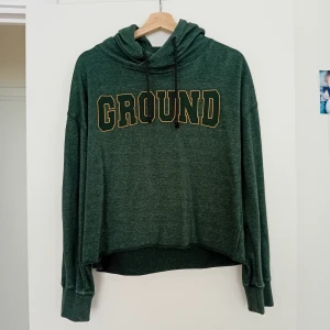 Grön hoodie S - Mörkgrön hoodie från lager 157 med stor gul text 'GROUND' på bröstet. Tröjan har huva med snörning, långa ärmar och en lite loose passform. Perfekt för chill dagar eller när du vill ha en sportig vibe.