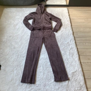 Juicy Couture brun velour set - Mysig brunt set från Juicy Couture i mjuk velour med dragkedja, huva och snörning och fickor . Klassisk JC-logo broderad på bröstet och framficka och stora fickor framtill. Perfekt för chill dagar men också perfekt för dagar ute