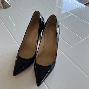 Svarta lackpumps från Christian Louboutin - Klassiska svarta pumps i lack från Christian Louboutin med ikonisk röd sula. Skorna har spetsig tå och hög klack, vilket ger en elegant och tidlös look. Perfekta för dig som vill sticka ut med exklusiv design och lyxig känsla.
