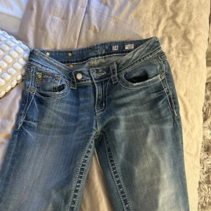 Miss Me bootcut jeans med broderi - Snygga blå bootcut jeans från Miss Me med ljus tvätt och kontrastsömmar. Bakfickorna har detaljerat broderi och nitar som ger extra edge. Klassisk dragkedja och metallknappar med logga. Perfekta för dig som gillar statement-jeans. De har extra knapp men den går att ta bort,