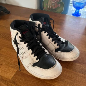 Nike svartvita sneakers str 43 - Säljer ett par Nike sneakers i svart och vitt med  röd Jumpman-logga på sidan. Skorna har perforerade detaljer, svart snörning och rund tå. Tillverkade i skinn med hög midcut och platt sula. Perfekt för dig som gillar streetstyle och basketvibe. Köpta på Zalando, stl 43