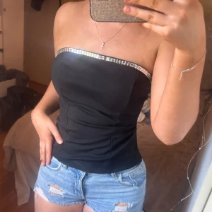 Svart tubtopp med glitter kant - Säljer en svart tubtopp med glittrig silvrig kant upptill. Helt ny från fashionnova, har prislapp kvar. I storlek xs/s.