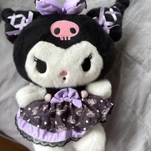 Kuromi gosedjur  - Supersöt Kuromi med svart botten, klänning med vita prickar och små Kuromi-figurer. Klänningen har en lila rosett framtill, volangkant och svarta spetsdetaljer. Perfekt för dig som älskar kawaii-stil och är en kuromi älskare!