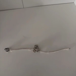 Pandora silverarmband med berlocker - Snyggt silverfärgat armband från Pandora med en berlock.. Armbandet har klassisk ormkedja och detaljerade charms som ger en personlig touch. Perfekt accessoar för att lyfta din stil. Aldrig använt men har ej lådan kvar då jag fick de som en present
