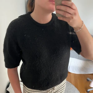 Svart stickad tröja med kort ärm - Säljer en svart stickad tröja med rund hals och korta ärmar. Tröjan har en mjuk och lite fluffig yta som ger en mysig känsla. Perfekt att matcha med jeans eller kjol för en chill look.
