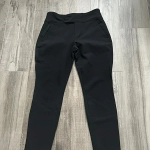 Svarta slim kostymbyxor - Svarta kostymbyxor med slim passform och hög midja. Byxorna har fickor fram med diskret dragkedja och fuskfickor bak. Materialet är mjukt och stretchigt, vilket gör dem riktigt bekväma. Perfekta för en clean och stilren look. De har en slitning i grenen, se bild 3.