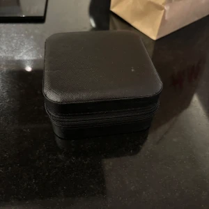 Svart smyckesask med dragkedja - Praktisk och stilren smyckesask i svart med dragkedja. Insidan är ljus och har flera fack för ringar, örhängen och halsband. Perfekt för att hålla koll på dina favoritsmycken när du är på språng eller vill ha ordning hemma. Aldrig använd 