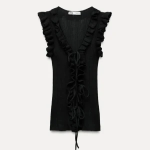 stickad topp - Snygg svart topp från Zara med volanger längs v-ringningen och framtill. Toppen har snörning framtill och är ärmlös med ribbad struktur. Perfekt för dig som gillar detaljer och vill sticka ut lite extra.