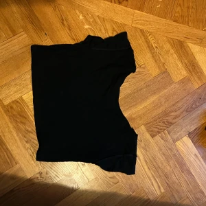 Svart oneshoulder topp - Säljer en svart oneshoulder topp med asymmetrisk design. Toppen är croppad och har en cool, modern look som passar perfekt till jeans eller kjol. Materialet känns mjukt och lätt mot huden, vilket gör den skön att bära. Perfekt för dig som gillar stilrena och trendiga plagg.