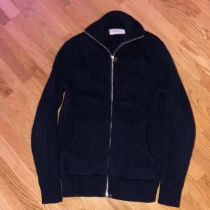 Svart stickad kofta från Zara - Svart stickad kofta från Zara med hel dragkedja framtill och hög krage. Tröjan har två fickor och är ribbstickad för en snygg struktur. Perfekt för lager-på-lager under kyliga dagar.
