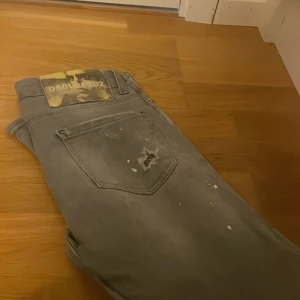 Grå jeans från Dsquared2 - Grå jeans från Dsquared2 med coola slitningar och färgstänk på bakfickan. Snyggt Dsquared2-märke i läder baktill. Jeansen har en rak passform och klassisk femficksdesign, perfekta för en avslappnad streetstil.