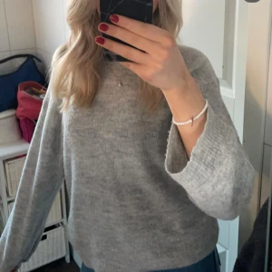 Grå stickad tröja med vida ärmar - Mysig grå stickad tröja med rund hals och vida, långa ärmar. Perfekt för kyliga dagar och enkel att matcha med jeans eller kjol. Tröjan har en avslappnad passform och är superbekväm att bära.