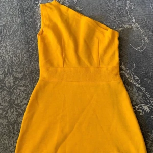 Gul oneshoulder klänning - Snygg gul klänning med oneshoulder-design och figurnära passform. Klänningen har markerad midja och är ärmlös på ena sidan, vilket ger en modern och trendig look. Perfekt för dig som vill sticka ut med färg och stil.