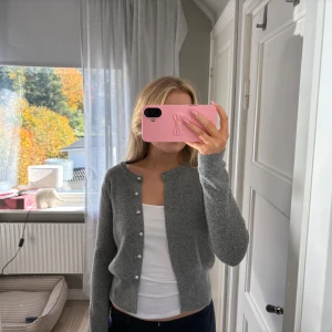 Grå kofta med pärlknappar - Superfin grå kofta med långa ärmar och snygga pärlknappar framtill. Koftan är stickad och har en klassisk, enkel design som passar perfekt till jeans eller kjol. Mjuk och skön att ha på sig under kyligare dagar.