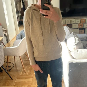Beige hoodie i mjuk bomull - Säljer en stilren beige hoodie med huva och snörning. Tröjan är i mjuk bomull och har långa ärmar samt ribbade muddar vid ärmslut och nederkant. Perfekt för en avslappnad look och passar året runt. Modellen är 172