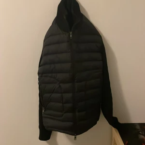 Svart quiltad cardiganjacka  - Snygg svart cardiganjacka från Blancheporte med quiltat framstycke och mjuka ärmar. Jackan har dragkedja framtill, två fickor med dragkedja och en praktisk huva. Perfekt för lager på lager och en clean look.