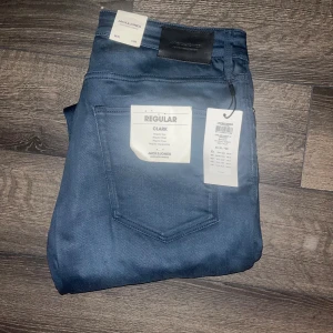 Jack & Jones jeans  - Helt nya !Snygga blå jeans från Jack & Jones, modell Clark Regular Fit. Klassisk femficksdesign med rak passform och normal midja. Jeansen är tillverkade i ett mjukt bomullsmaterial med lite stretch för extra komfort. Perfekta för en avslappnad och stilren look. Midja 45cm, längd 112cm. 