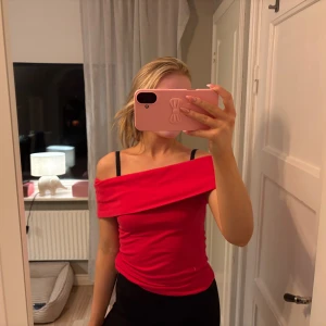Röd offshoulder topp - Säljer en snygg röd offshoulder topp med bred omlottkrage. Toppen är figurnära och har en cool, axelbar design som ger en trendig vibe. Perfekt för dig som vill sticka ut med en färgstark och modern look.
