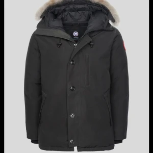 Canada Goose chateau  - Säljer en svart dunjacka från Canada Goose. Jackan har knappar, dragkedja och flera fickor. Perfekt för kalla dagar med sin tjocka och värmande design. Klassisk röd logga på ärmen och justerbar huva. Den kommer utan päls. Storleken är Xs men den passar dig som har S eller M i storlek ännu bättre eftersom den är lång.